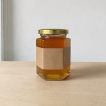 A jar of honey photographed plainly in daylight on a wooden table.
